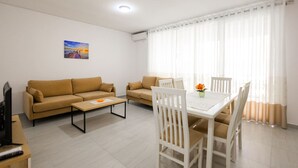A living room with two sofas, a coffee table, a TV, and a dining area with chairs and a table. - SanPietro Vacation Apartment 042 (Plazhi San Pietro)