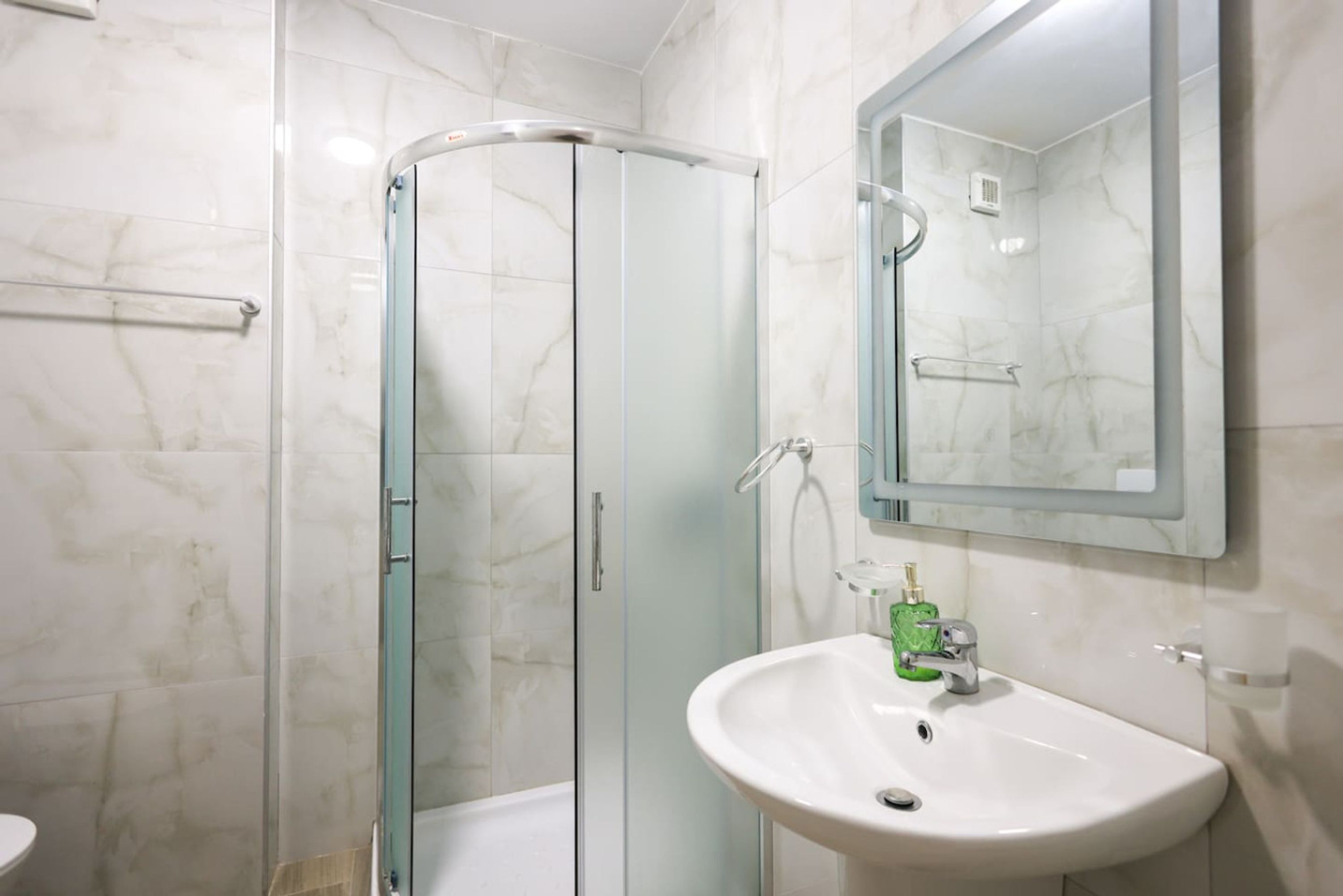 A modern bathroom with a glass shower enclosure, a white sink, and a mirror above it.