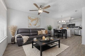 Ein modernes Wohnzimmer mit einem dunkelbraunen Ledersofa, einem Couchtisch mit Kerzen und einem Deckenventilator.