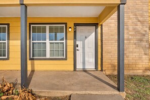 Un bâtiment jaune avec une porte et des fenêtres blanches, un porche en béton et un mur en briques.