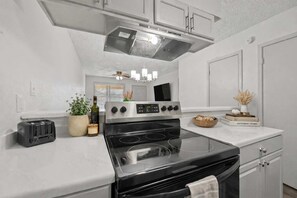 Una cucina moderna con piano cottura nero, ripiani bianchi e mobili in acciaio inossidabile.