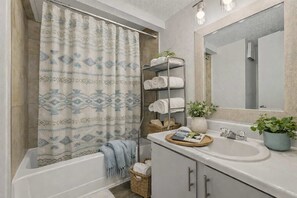Une salle de bain moderne avec un rideau de douche, un porte-serviettes, un lavabo, un miroir et une plante en pot.
