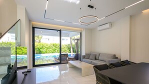 A modern living room with a glass door leading to a pool, a sofa, a coffee table, and a dining area.