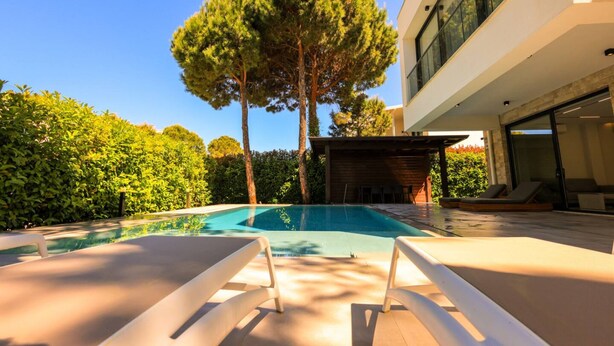 A modern outdoor pool area with lounge chairs, a wooden deck, and a building with large windows.