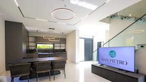 A modern kitchen with a dining area, a TV displaying 'SAN PIEDRO Vacation Rentals', and a staircase leading to an upper level.