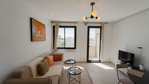 A modern living room with a sofa, two side tables, a television, and a view through a door. - Petit Cocon Neuf et Stylé à la Marsa (Marsa)