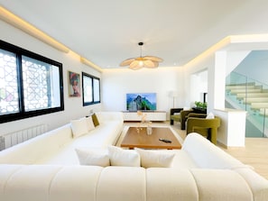 A modern living room with a white sofa, a wooden coffee table, and a large flat-screen TV. - Villa Ambre : détente, piscine privée & hammam (La Marsa)