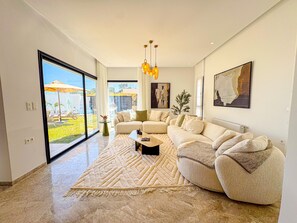 A modern living room with a large sectional sofa, a coffee table, and a view of a garden through large windows. - villa Alba: luxe et confort a Hammamet (Mrezga)