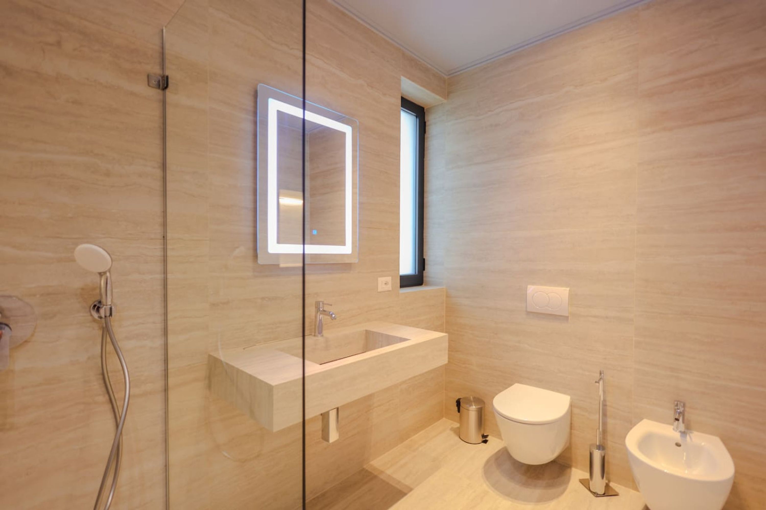 Ein modernes Badezimmer mit einer Glaskabine zur Dusche, einem großen Spiegel, einem Waschbecken, einer Toilette und einem Bidet.