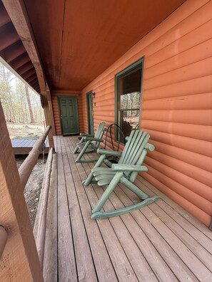 A wooden porch with rocking chairs, a door, and windows.