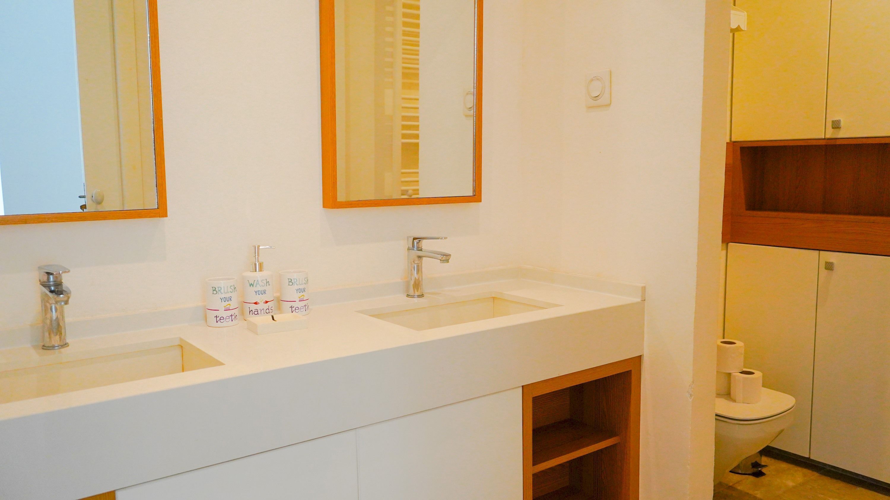 A bathroom with two sinks, a mirror, and a toilet.