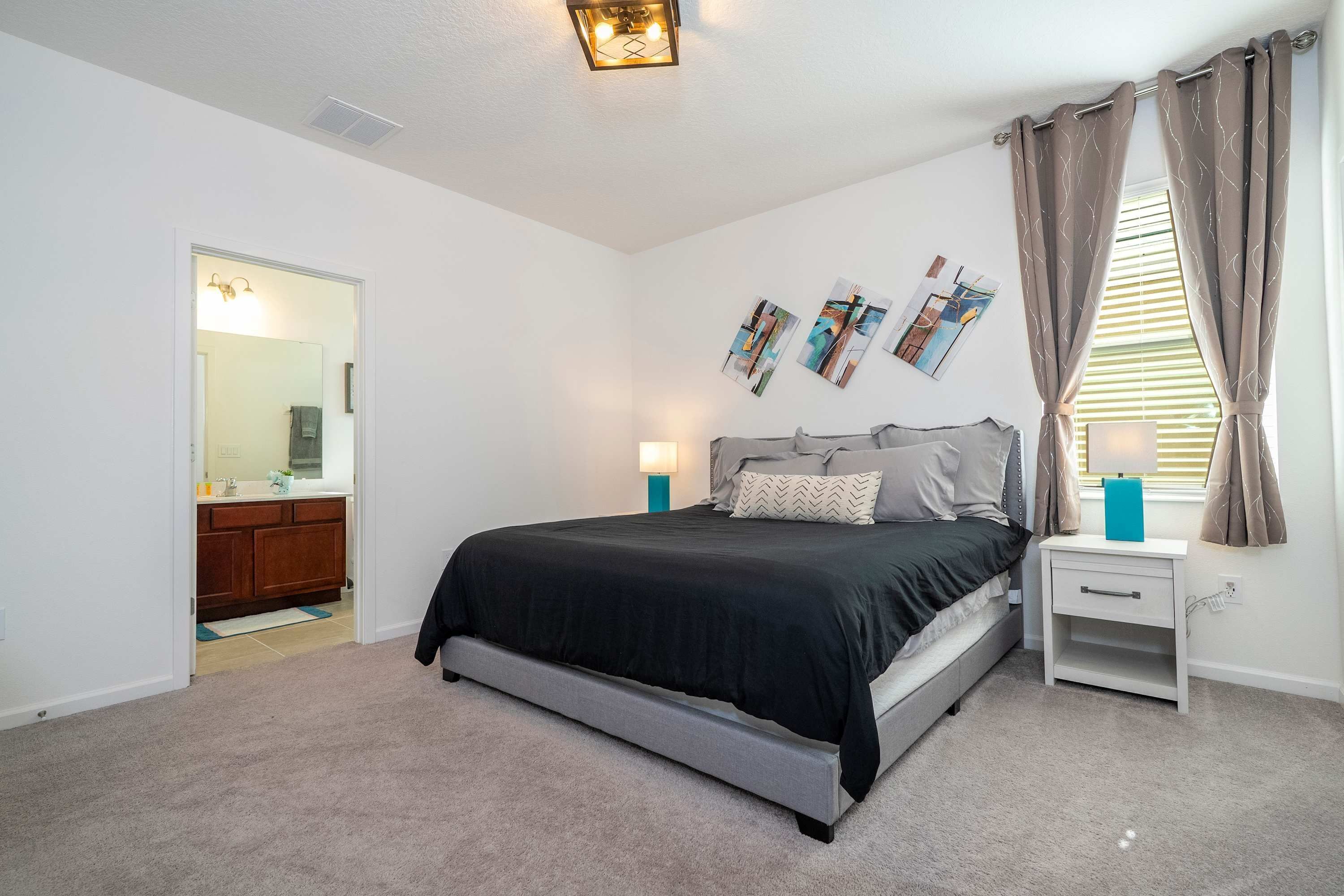 A bedroom with a bed, bedside tables, a nightstand, a mirror, and artwork on the wall.