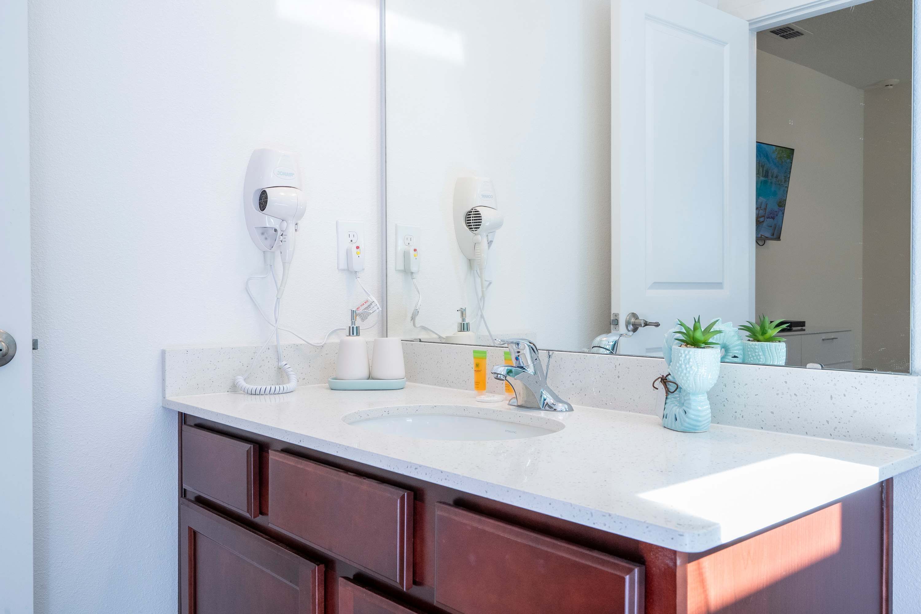 A bathroom with a white sink, two hair dryers, a mirror, and a door.