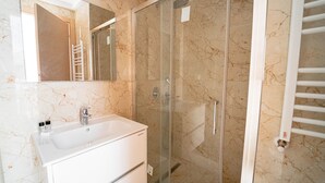 Un baño con un lavamanos blanco, una ducha con mampara de cristal y una pared de mármol.