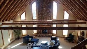A spacious loft with a stone fireplace, wooden beams, and large windows. - Luxurious 4-bedroom cabin that sleeps 13 close to Cooperstown NY with AC (Burlington Flats)