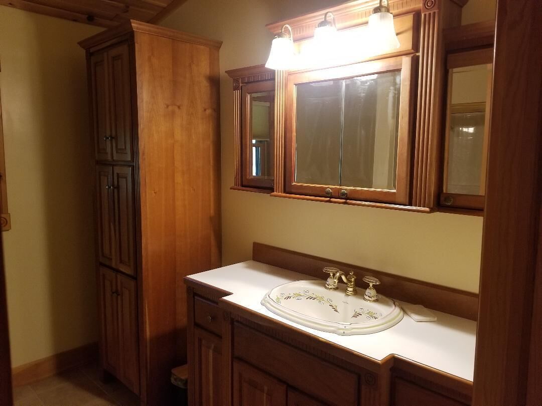 A bathroom with a wooden vanity, a white sink with a decorative glass cover, and a mirror with two lights above it.