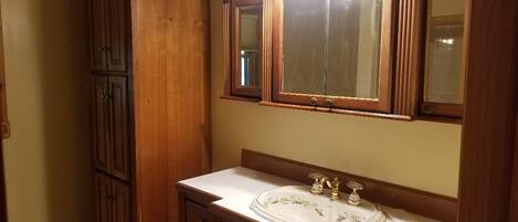 A bathroom with a wooden vanity, a white sink with a decorative glass cover, and a mirror with two lights above it.