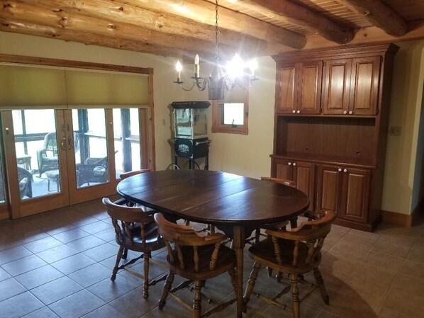 A dining area with a round wooden table and four chairs, a chandelier, wooden cabinets, and a sliding glass door leading to an outdoor patio.