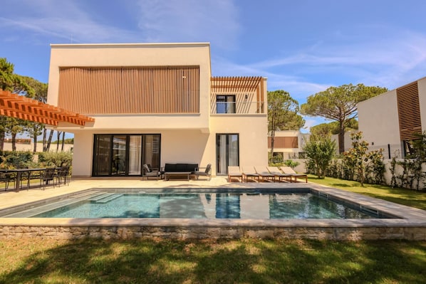 A modern two-story house with a swimming pool, outdoor seating, and a pergola.
