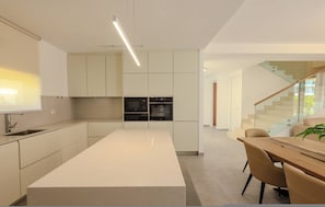 A modern kitchen with integrated appliances, a central island, and a dining area with a wooden table and chairs.