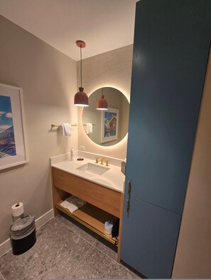 A modern bathroom with a white sink, gold faucets, and a round mirror with a circular light. - Go! 29 Margaritaville Studio (Kissimmee)