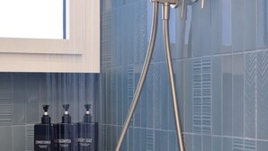 Eine Dusche mit Handbrause, Wandarmatur und drei Flaschen Badesseife auf einem Regal.