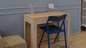 Ein kleiner, ordentlicher Raum mit Schreibtisch und Stuhl, einer Wandleuchte und einem Heizkörper.