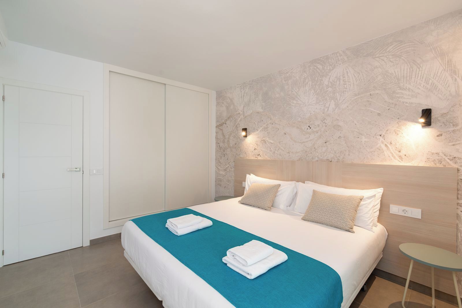 Ein Hotelzimmer mit einem Bett, einer blauen Akzentwand, einem weißen Kleiderschrank und einem kleinen Tisch.