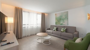 Ein modernes Hotelzimmer mit einer Couch, einem runden Tisch, einem Fernseher und einem Gemälde an der Wand.