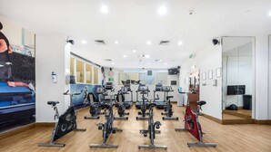 Ein Fitnessraum mit mehreren Ergometer, einem großen Spiegel und Holzboden.