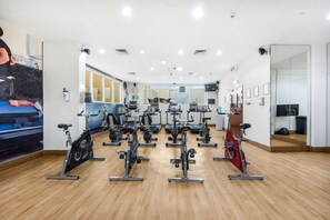 A gym with multiple stationary bikes, a large mirror, and a wooden floor. - Free Housekeeping Visits During Your Stay - Stayshort - Cozy 1BR Retreat in JLT That Sleeps 4 (Dubai)