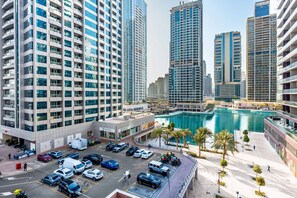 A modern urban area with high-rise buildings, a central swimming pool, and a parking lot with various vehicles. - Free Housekeeping Visits During Your Stay - Stayshort - Cozy 1BR Retreat in JLT That Sleeps 4 (Dubai)