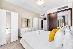 A modern hotel room with a large bed, white bedding, a mirror, a wardrobe, and a bathroom visible through an open door. - Free Housekeeping Visits During Your Stay - Stayshort - Chic 1BR Retreat in Dubai Marina That Sleeps 4 (Dubai)