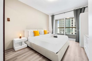 Ein modernes Hotelzimmer mit einem großen Bett, einem Nachttisch mit Lampe, einem Kleiderschrank und Blick auf die Stadt durch große Fenster.