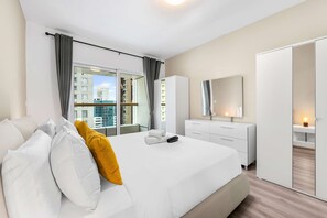 Ein modernes Hotelzimmer mit einem großen Bett, einem Kleiderschrank, einem Nachttisch mit Lampe und Blick auf die Stadt durch große Fenster.