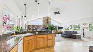 A spacious kitchen with granite countertops, wooden cabinets, and a large island. There is a stone fireplace, a bookshelf, and a seating area with a sofa and coffee table. - NEW! Pool, BBQ, Beach Access, Hot Tub, Gym (SDreaming) (Westport)