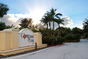 A sign for Compass Bay with a curved top and a star emblem, surrounded by palm trees and a clear sky. - Modern 4BR w  Patio   Resort Pool   Compass Bay (Kissimmee)