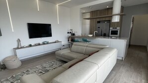 A modern living room with a large L-shaped sofa, a flat-screen TV mounted on the wall, and a kitchen area with a built-in oven and microwave. - Attico con splendida vista su Villa Ada (Roma (RM))