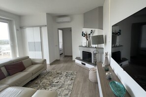 Uma sala de estar moderna com um sofá bege, um tapete estampado, uma lareira e uma televisão grande.