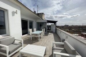 Eine Dachterrasse mit Tisch und Stühlen, einer Sitzecke und Blick auf die Stadt.
