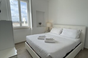 Cama bem arrumada com lençóis e toalhas brancos, abajur e janela com vista do céu.
