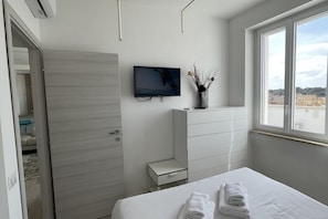 Ein modernes Schlafzimmer mit Bett, Fernseher, Kommode und Fenster mit Blick auf die Stadt.