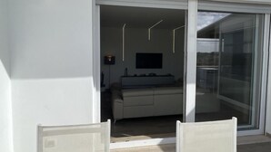 A balcony with two chairs, a sliding glass door leading to a living area with a sofa and a TV. - Attico con splendida vista su Villa Ada (Roma (RM))