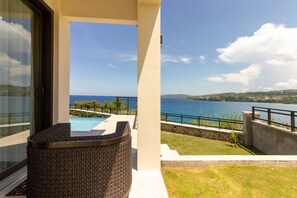A balcony with a view of the sea, a pool, and a wicker chair. - Ocean's Edge ~ Fully Staffed ~ Luxury Villa (Tower Isle)