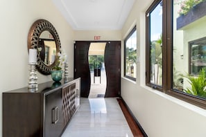 A hallway with a dark wooden cabinet, a large mirror, and a view of the outdoors through a window. - Ocean's Edge ~ Fully Staffed ~ Luxury Villa (Tower Isle)