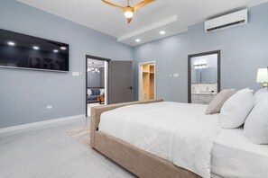 A modern bedroom with a large bed, a ceiling fan, an air conditioning unit, a TV mounted on the wall, and a walk-in closet. - Coastal Escape in Riviera, Tower Isle~Beach Nearby (Tower Isle)