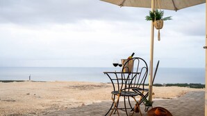 Een strandtafel met een stoel, een fles, glazen, een hoed en een hangplant.
