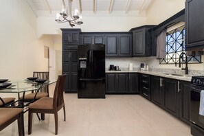 A modern kitchen with dark cabinetry, a glass dining table, and a built-in oven. - 5 BedRmOasis DraxHall~Pool~Gym~ (Saint Ann's Bay)