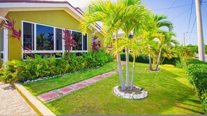 A yellow house with a well-maintained garden, including palm trees and a paved pathway. - Adorable Beach House in Drax Hall~Gated~Pool~Gym (Saint Ann's Bay)