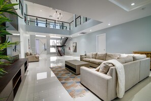 A spacious living area with a high ceiling, a staircase leading to an upper level, a large beige sofa, a coffee table, and a patterned rug. - Luxury Oceanfront Villa~ Fully Staffed~Pool~Jacuzzi~Movie Theatre (Tower Isle)